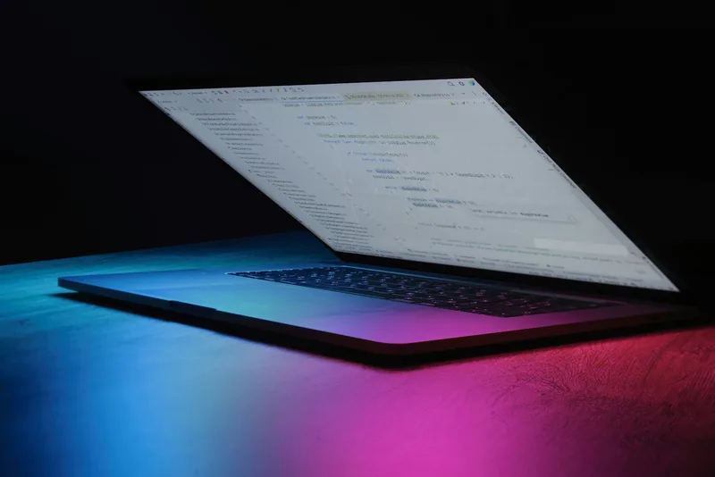 Laptop showing a code editor, lit by blue and pink ambient light